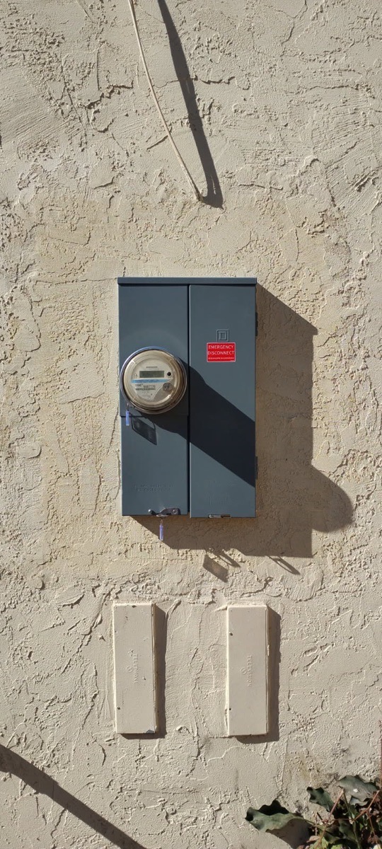 Dark exterior meter-panel cabinet surrounded by continuous textured color-coat stucco