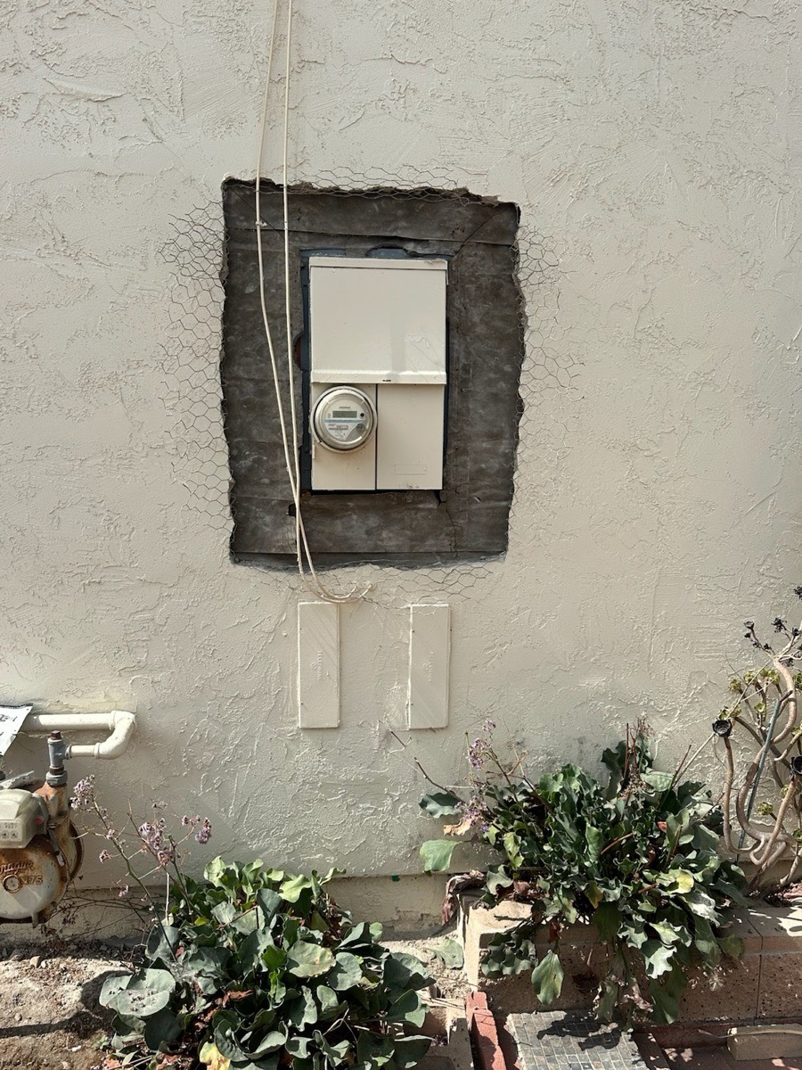 Existing exterior meter-panel cabinet with opened stucco perimeter and visible lath